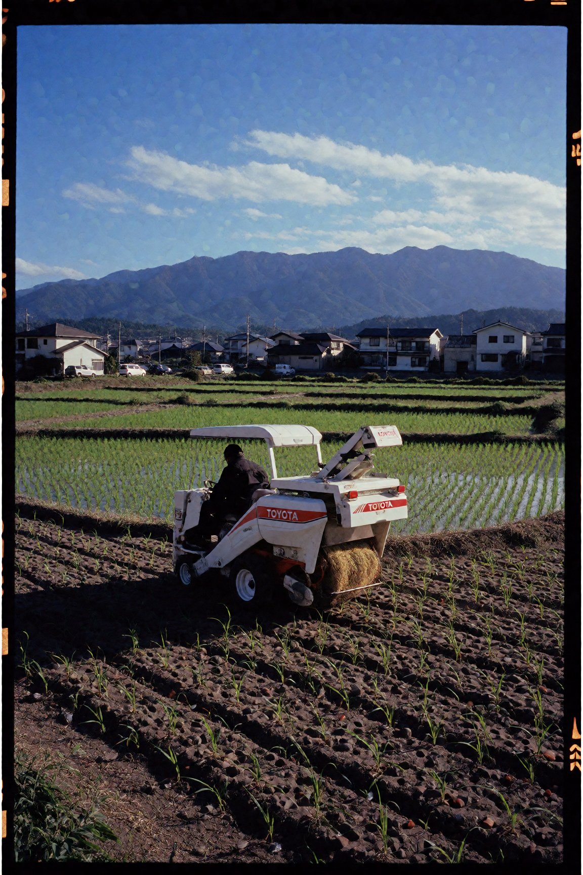 toyota rice sowing machine,  ride on,  quiet rural scene in a japanese town with a view of the mountains in the distance b...