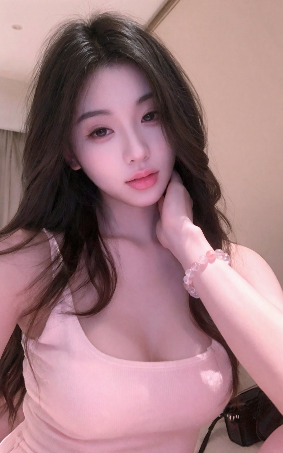 The image is a photograph of a young woman taking a close-up selfie. She has light skin,  long brown hair with soft waves,...