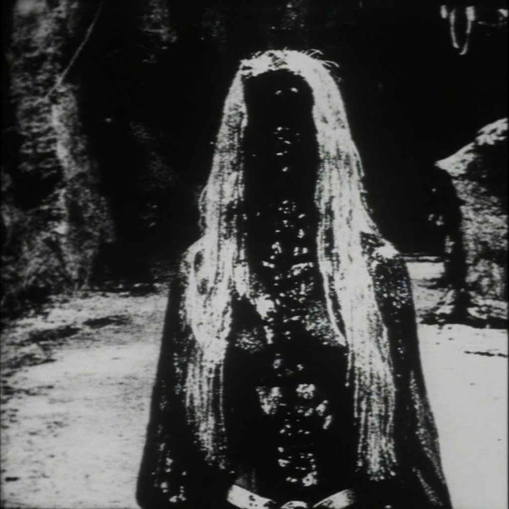 woman standing on a dark roadside at night,  her long pale hair hanging straight; where her face should be is a smooth bla...