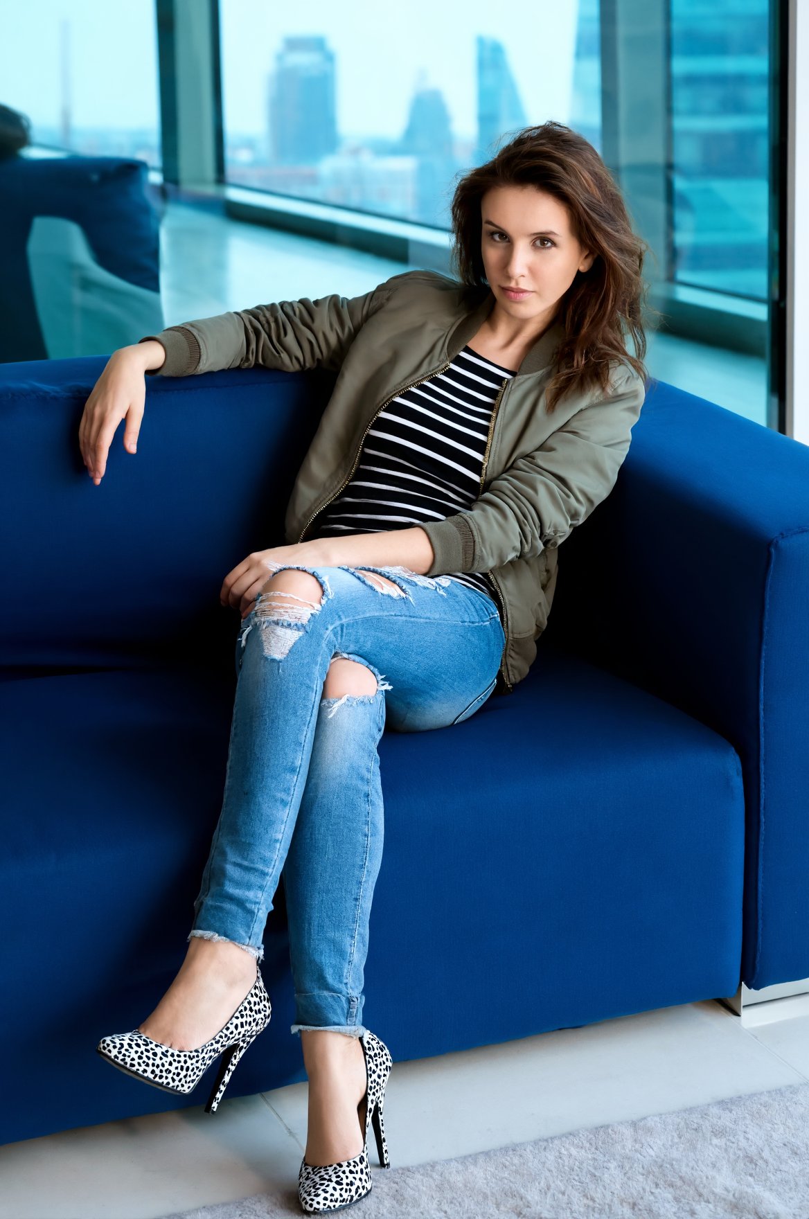 wo4l1sr3 lounging on a plush,  deep blue sofa in a modern,  urban setting with large windows showcasing a cityscape in the...