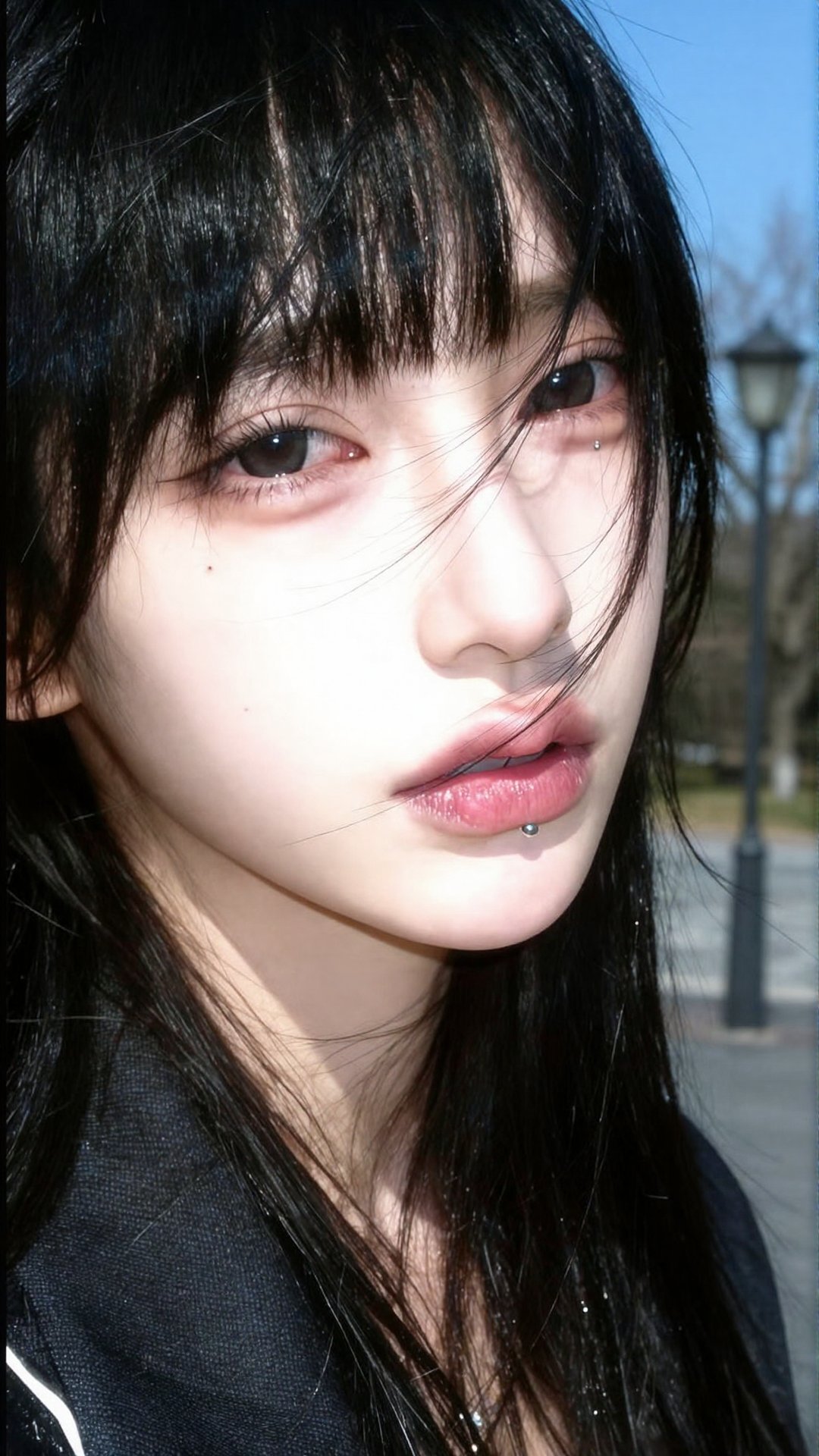 A close-up portrait focusing strictly on the face of a pale young woman with very long black hair and bangs blowing across...