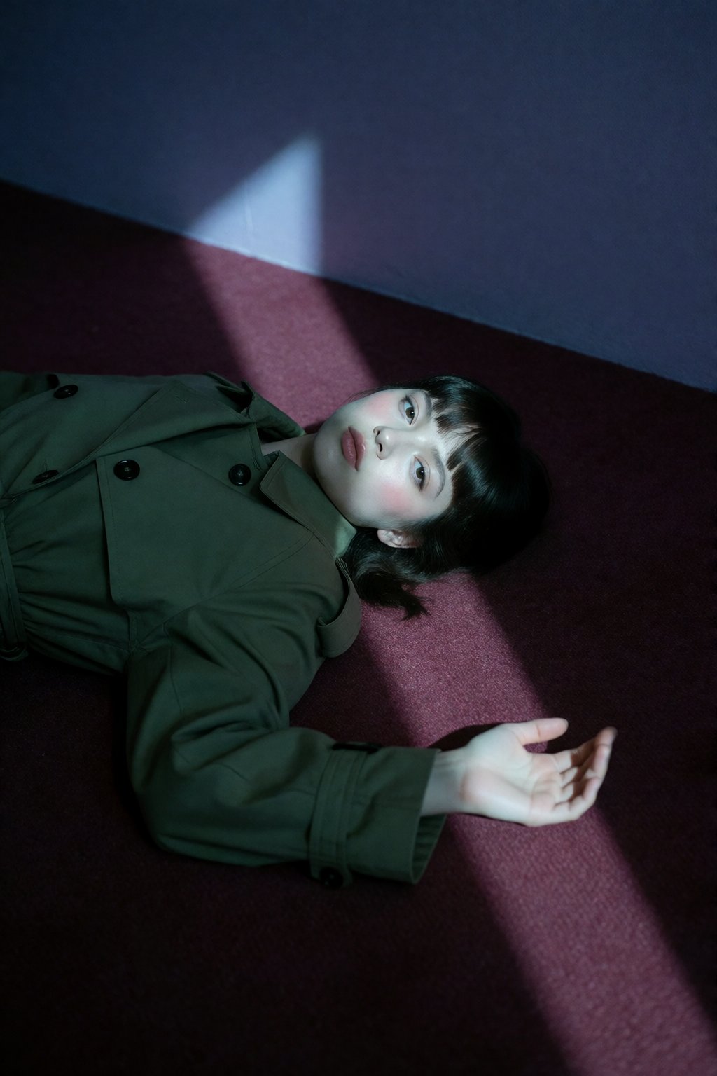 A young woman with blunt dark bangs lies on a burgundy carpet illuminated by a sharp,  geometric beam of cool light. Weari...