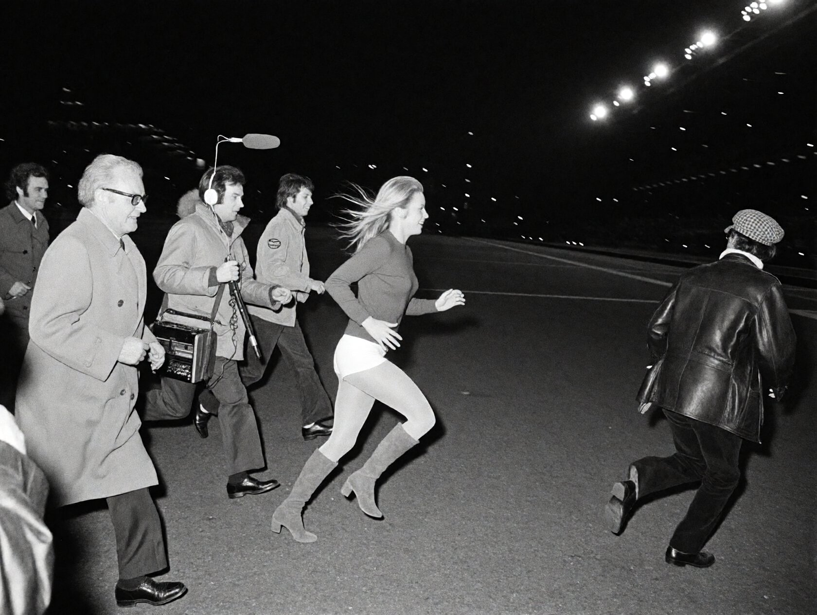 {"high_level_description":"A grain-heavy 1970s black and white photograph captures a blonde woman in mid-stride,  fleeing...
