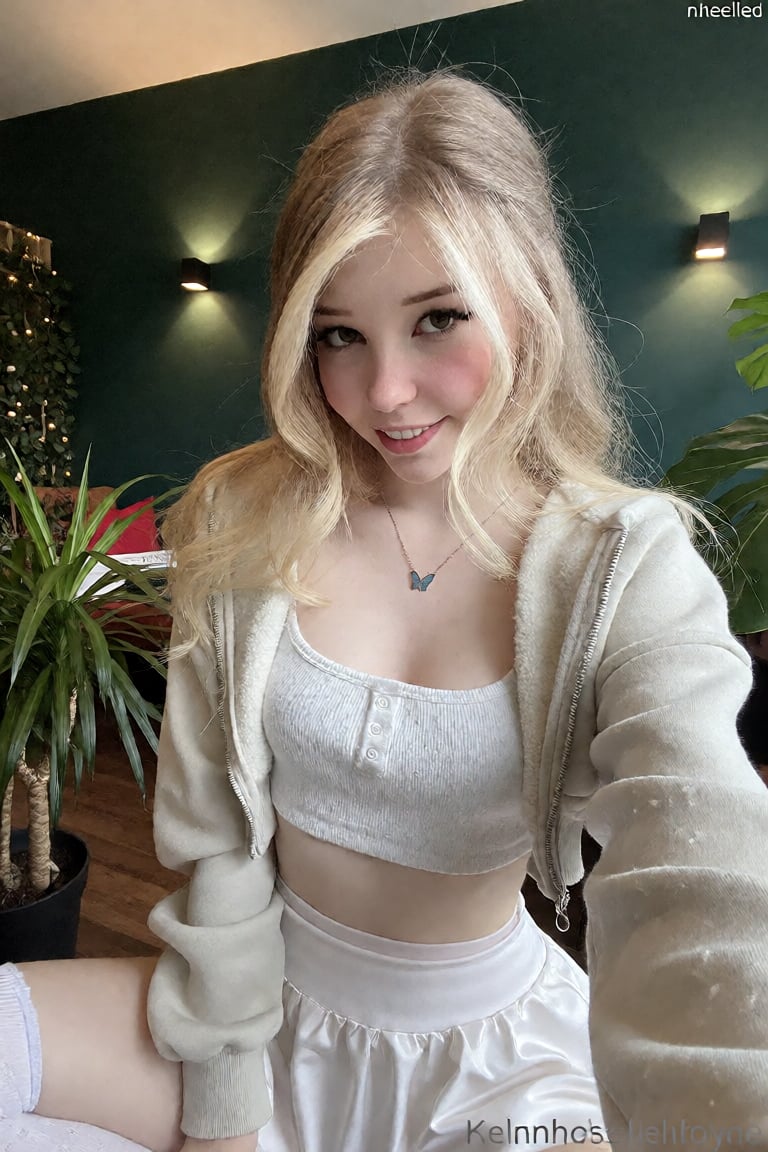 Blonde hair,  The image shows a young woman sitting indoors,  surrounded by lush green plants. She is wearing a white crop...