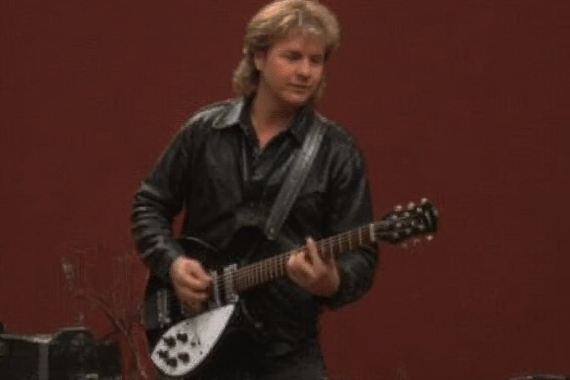 Roger Whisner,1boy,solo,front view,half body, standing,Rickenbacker,electric guitar, playing guitar in a nightcub on stage, long hair, black leather jacket, van dyke