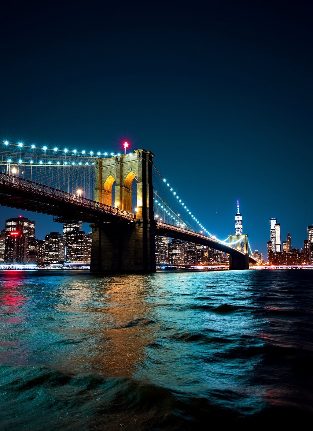 This is a stunning nighttime photograph capturing the Brooklyn Bridge from a vantage point on the water,  likely from a bo...