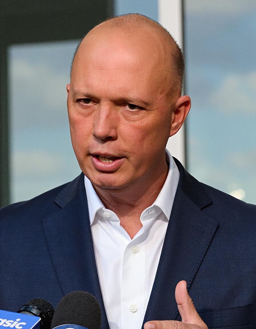 A photograph of a man with a clean-shaven head,  wearing a dark blue suit and a crisp white shirt,  addressing reporters a...