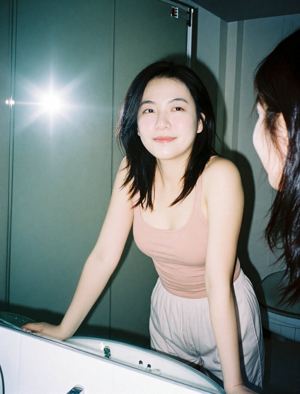 A young woman with the same unchanged face,  pale soft complexion blown slightly by harsh 90s disposable-camera flash. Loo...