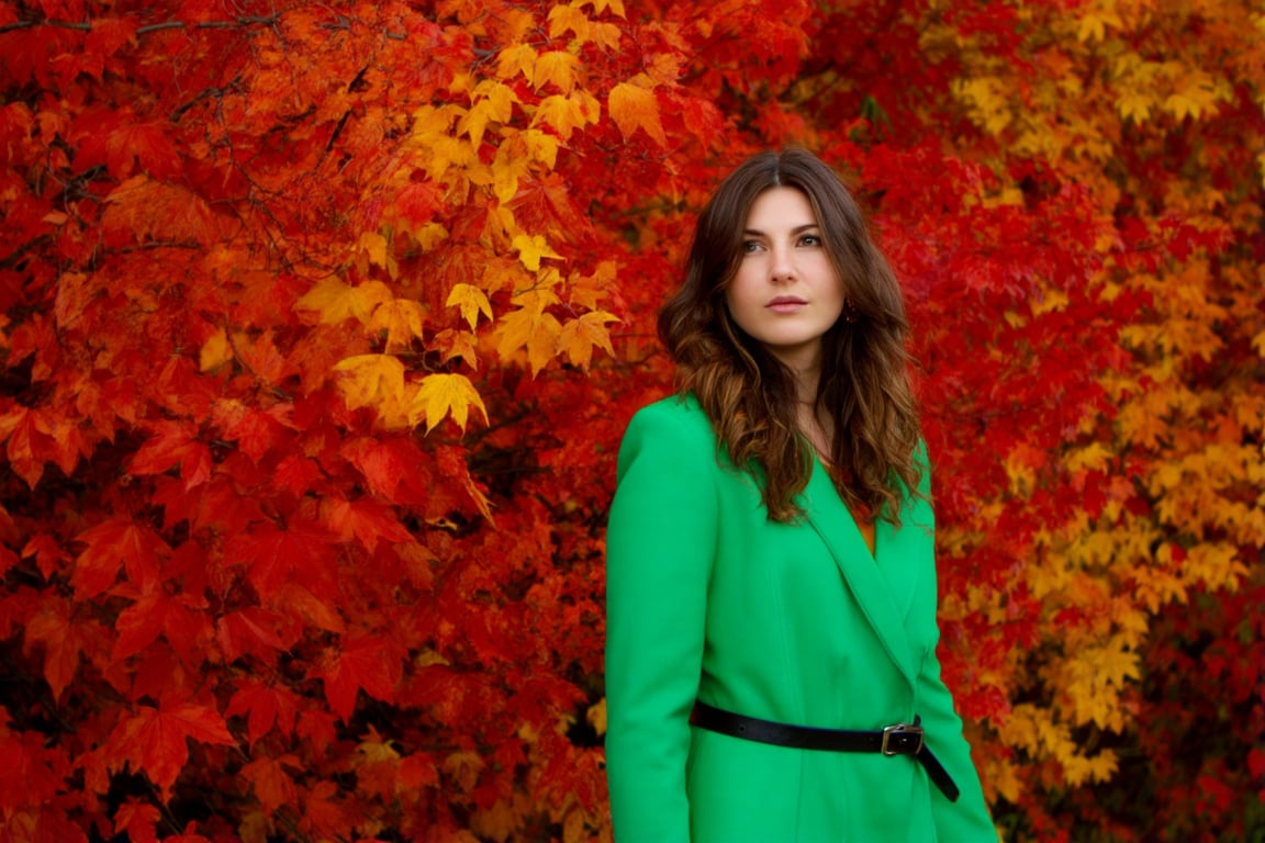 The image features a woman standing amidst a vibrant display of autumn foliage. She is dressed in a bright green jacket,...