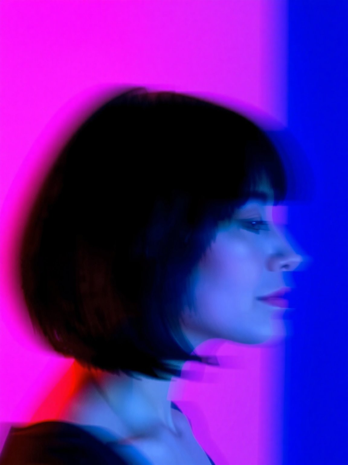 A blurred profile of a person with shoulder-length dark hair,  set against a vibrant,  abstract background. The lighting c...