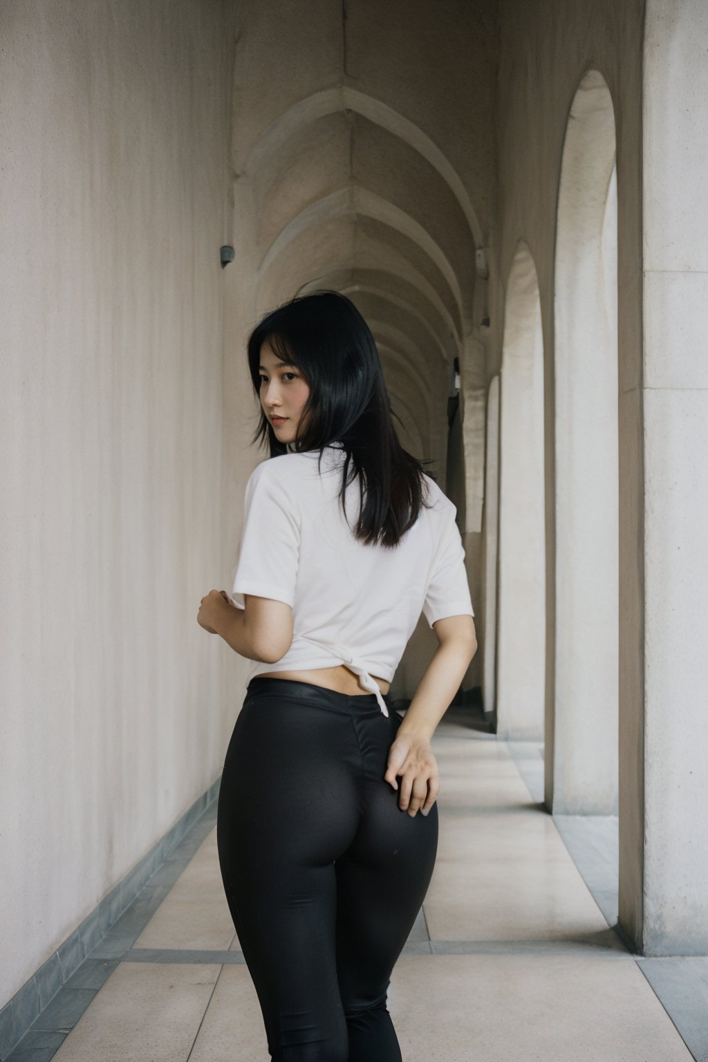 A photorealistic full-frame image of a petite Indo-Chinese girl striding confidently down a dimly lit corridor with beige walls and a marble floor. Her short jet-black hair is styled in two small pigtails tied with thin ribbons, positioned on the sides of her head. She is wearing a tight-fitting beige t-shirt that reaches her hips and long black leggings that clearly accentuate her shapely buttocks and rounded thighs as she walks away from the viewer. The camera captures her round face featuring a small round nose and plump lips hinting at a subtle smile, framed to emphasize her confident stride. The overall scene should convey a sense of motion and confidence, with high resolution and ultra-detailed quality