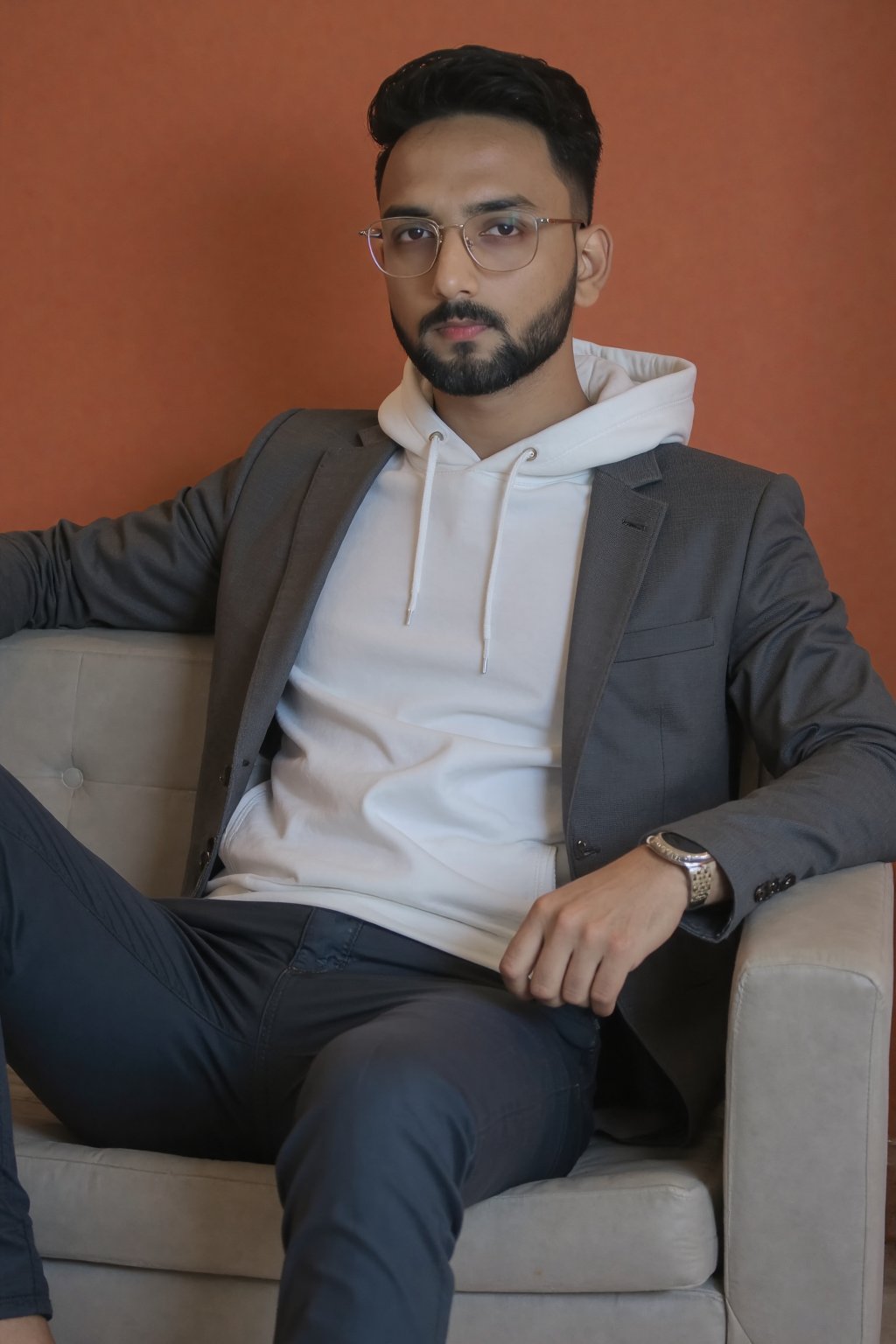 A stylish young man with short dark hair,  a well-groomed beard,  and a confident expression lounges on a modern gray couc...
