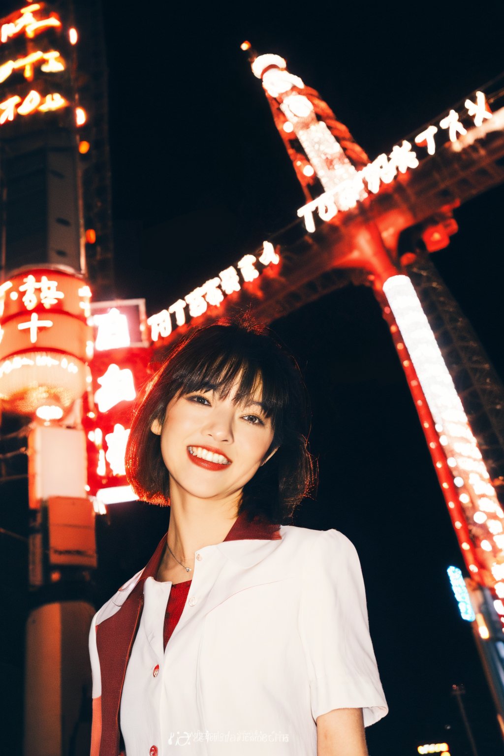 A young Asian woman, short hair, wearing a red jacket and a white t-shirt with Japanese text, necklace, standing on a Tokyo street at night, with Tokyo Tower in the background, illuminated city lights, red lanterns, urban style, night photography, candid pose, low angle shot, with a hint of film grain.

,fujifilm