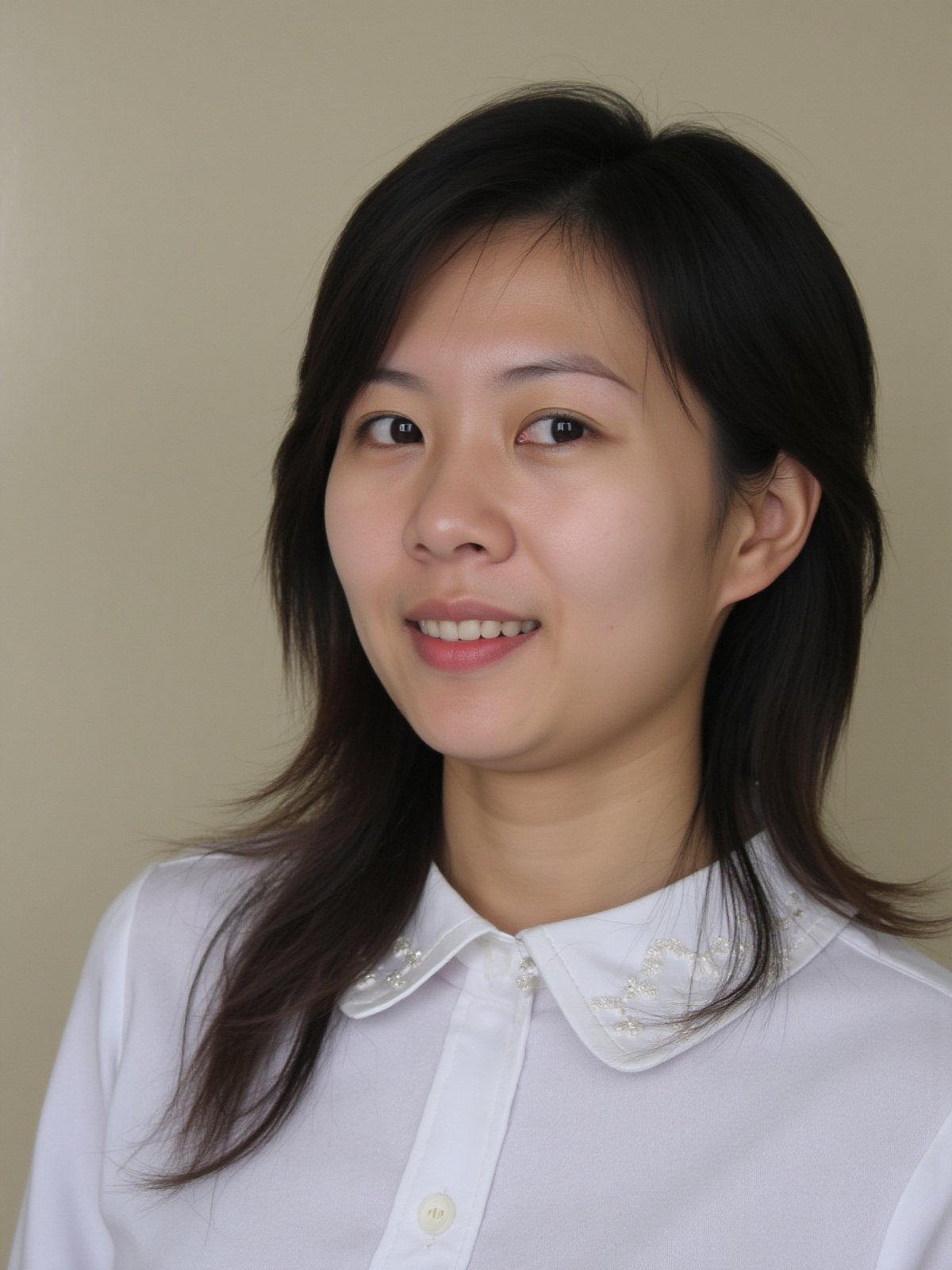 A close-up shot of a young Asian woman with long dark brown hair and brown eyes. She is wearing a white collared button down shirt with white embroidery on the collar. Her lips are a vibrant shade of pink. Her eyebrows are a light brown and her eyes are a darker shade of brown. She has a slight smile on her face. The backdrop is a light beige wall.