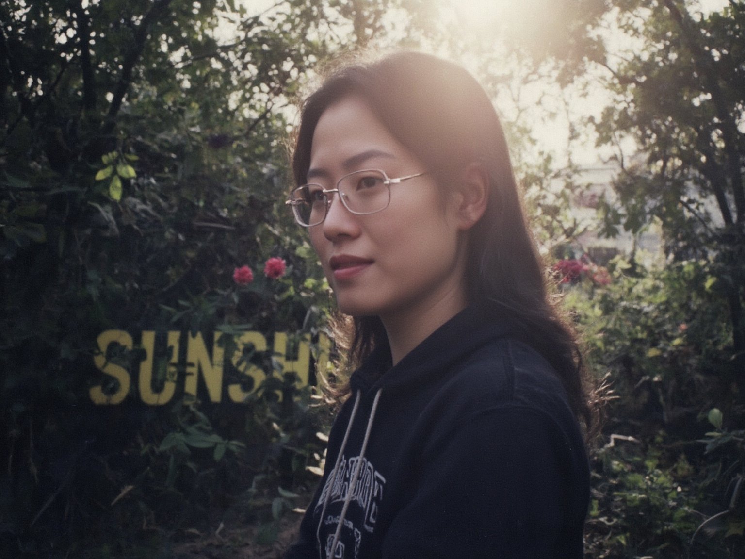 Floodlight,This is a sunlit portrait of a young boy in profile with he face to the camera,glasses,bathed in warm,soft light that creates a halo effect around he. He black hair . He is wearing sportswear, The background is blurred to ensure that the focus is on the subject. The photograph is softly lit and luminous,with delicate romantic tones and an ethereal,dreamy quality. The soft focus enhances the gentle and serene atmosphere of the image., where lush greenery and bold emblazoned words" SUNSHINE "create a striking visual counterpoint to her melancholic countenance, as if bathed in the faint light of the street lamps.(Film grain: 1.2, ultra detailed skin texture)