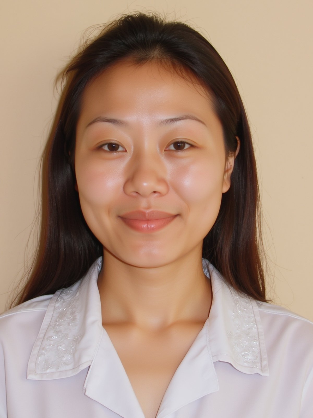 A close-up shot of a young Asian woman with long dark brown hair and brown eyes. She is wearing a white collared button down shirt with white embroidery on the collar. Her lips are a vibrant shade of pink. Her eyebrows are a light brown and her eyes are a darker shade of brown. She has a slight smile on her face. The backdrop is a light beige wall.


