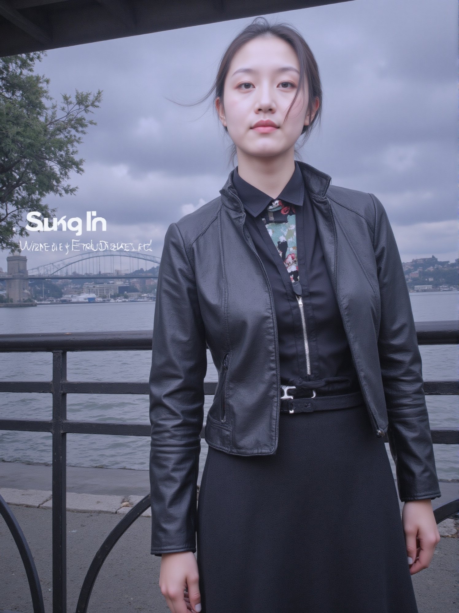 Captured on a digital screen, a woman stands in front of a body of water. She is dressed in a black leather jacket, a black skirt, and a black belt. Her hair is styled in a sleek bob, and her eyes are focused on the camera. The woman's hair is dark brown, and she is wearing a pair of black laces. The backdrop is a cloudy sky, and there is a bridge in the distance. To the left of the woman is a tree with green leaves, and the word "SUNSHINE" is visible in the top left corner of the screen. Below the screen, the words "Weekly Best Dressed" are written in white.