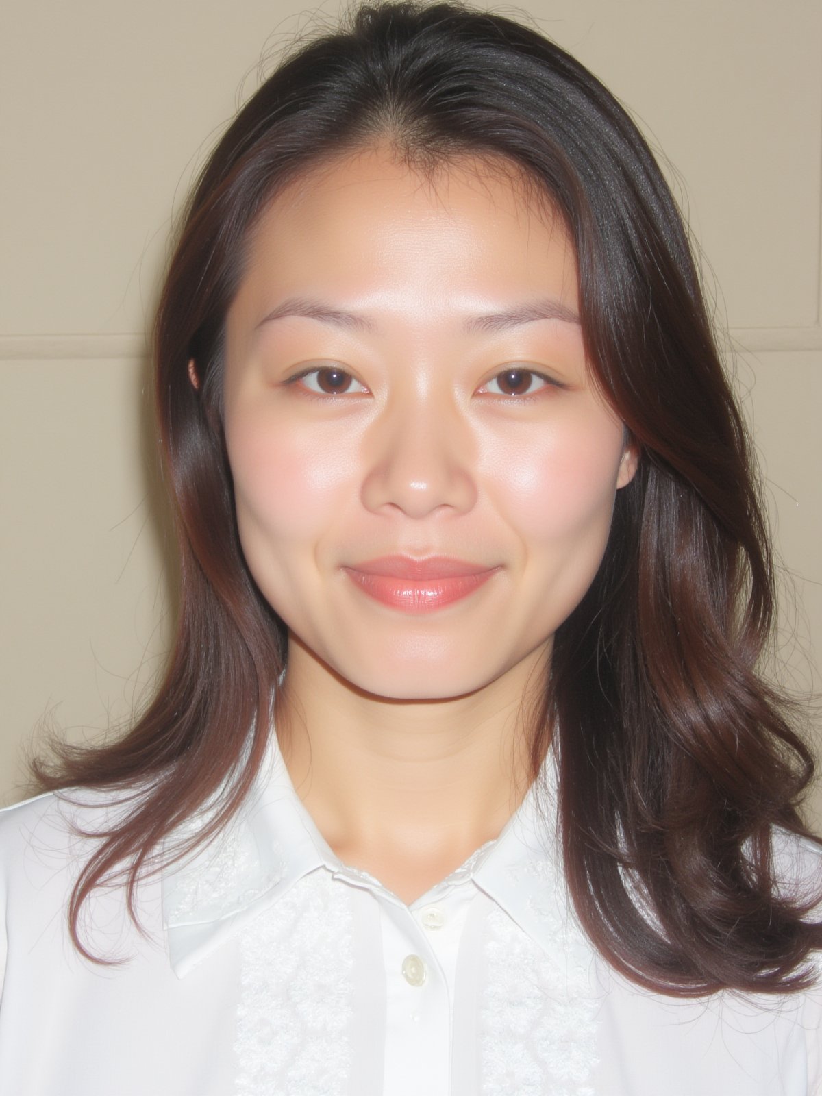 A close-up shot of a young Asian woman with long dark brown hair and brown eyes. She is wearing a white collared button down shirt with white embroidery on the collar. Her lips are a vibrant shade of pink. Her eyebrows are a light brown and her eyes are a darker shade of brown. She has a slight smile on her face. The backdrop is a light beige wall.