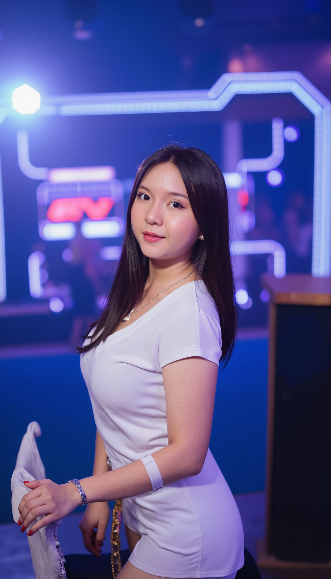 a woman with long dark brown hair, wearing a white short-sleeved polo shirt and a brown belt. She is standing in front of a backdrop of neon lights, a white chair, and a blue wall. She has a silver necklace around her neck and a white bandage on her left wrist. Her left hand is resting on the chair, while her right hand rests on the arm of the chair.