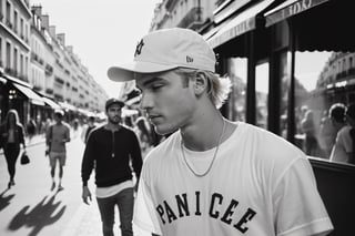 Street photography of a handsome young man, blond hair, wearing light summer juvenile clothing and wearing a baseball cap backwards position, in Paris under the gentle light of the golden hour, from a candid angle across the street, capturing everyday life in a monochromatic palette, taken in 35mm with Ilford XP2 400 film,photo r3al