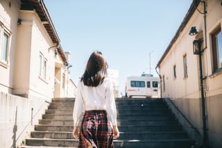 1girl, instagram photo, white shirt, solo, long hair, skirt, bangs, black hair, outdoors, plaid, from behind, plaid skirt, building, walking, stairs, real world location,japan,dream_girl,film_grain