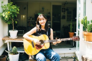 1girl, solo, long hair, messy hair, black hair, ((warm smile:0.7)), sitting, flower, sleeveless, looking at viewer, pants, indoors, ((detailed interior)), window, plant, denim, instrument, jeans, music, guitar, potted plant, japanese style, playing instrument, shelf, poster \(object\), flower pot, cactus, acoustic guitar