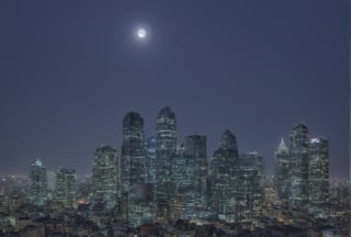 night, cloud lumened by city, bright moon, dark-gray-purple sky; sky scrapers square and rectangular skyscrapers with white frequent square windows, shades of skyscraper windows: dark blue, dark turquoise. The roofs of skyscrapers from dark squares or illuminated with a dim blue border,