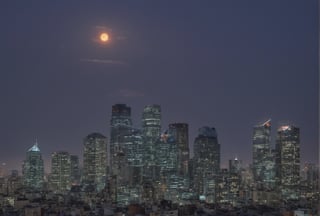 night, dark-orange cloud lumened by city, bright moon, dark-gray-purple sky; sky scrapers square and rectangular skyscrapers with white frequent square windows, shades of skyscraper windows: dark blue, dark turquoise. The roofs of skyscrapers from dark squares or illuminated with a dim blue border,